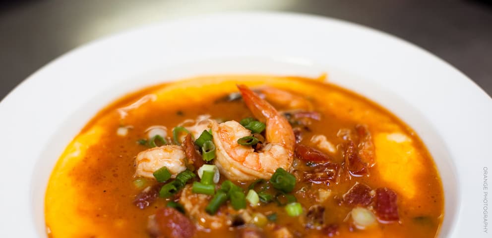 A bowl of shrimp and grits at Brenda's: whole shrimp in a tomato-based sauce over creamy grits, topped with sliced scallions.